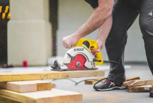 man in black sweatpants using DEWALT circular saw and cutting a wood plank